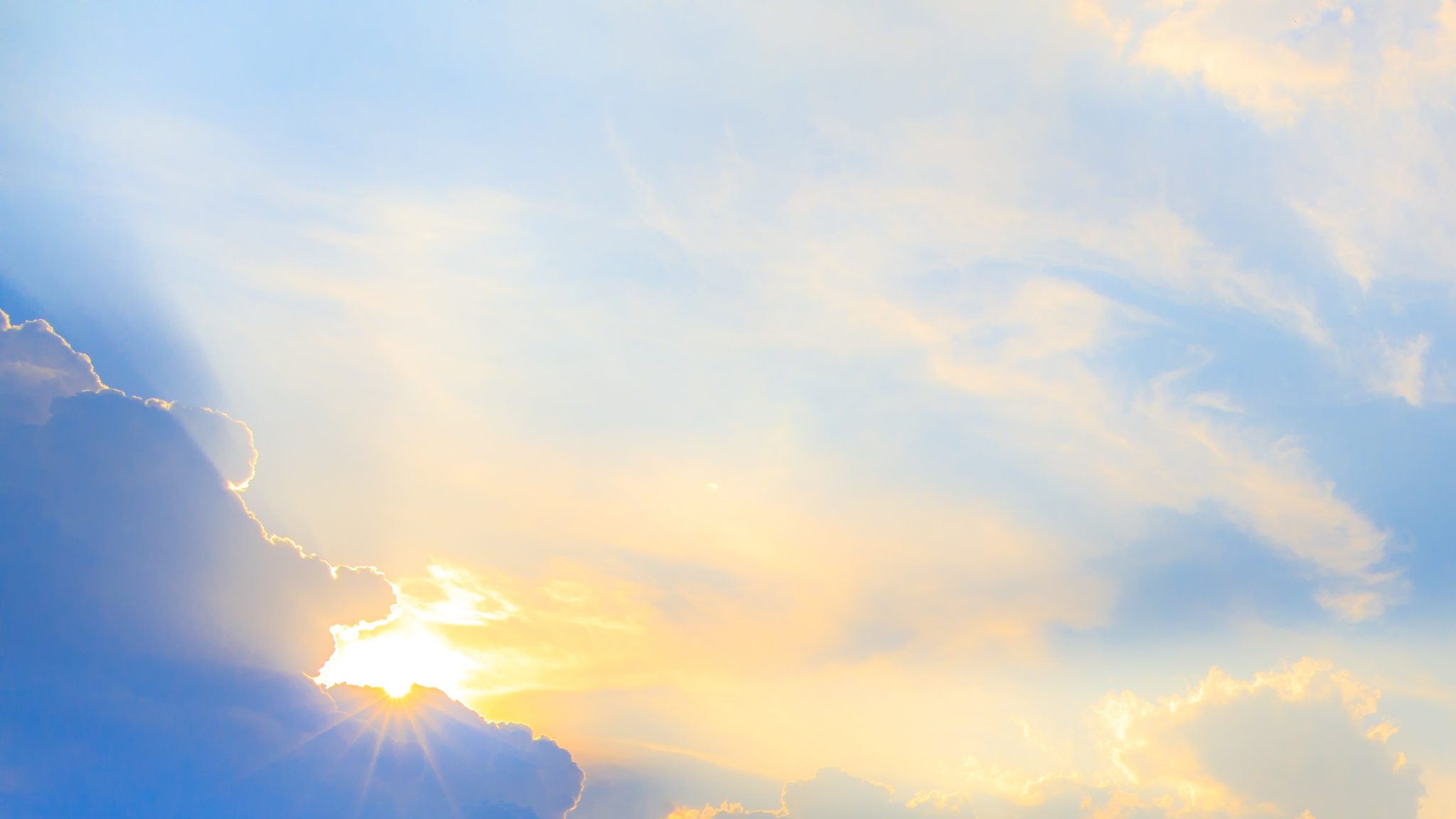 Pastel skyscape with sun peeking out behind clouds